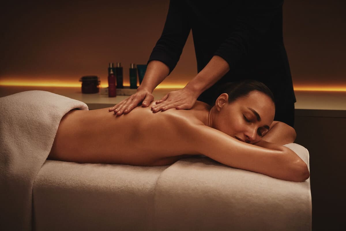Relaxing back massage treatment at Waterfall Spa in Ambleside Salutation Hotel featuring Elemis aromatherapy products, warm ambient lighting with golden glow, professional therapist performing therapeutic massage in tranquil treatment room in central Lake District location