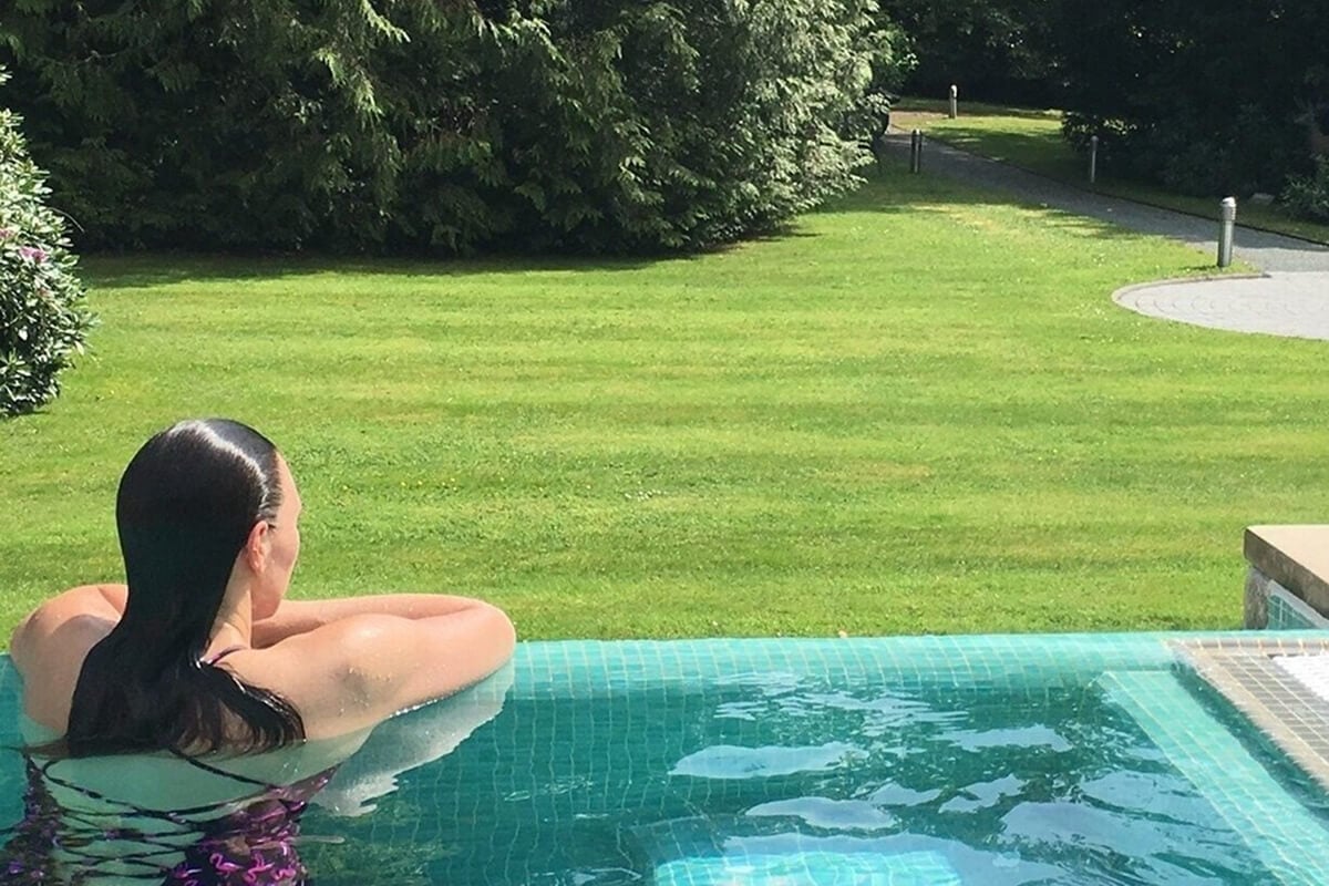 Guest relaxing in outdoor infinity pool at Armathwaite Hall Hotel and Spa near Bassenthwaite Lake, overlooking manicured parkland lawns and ancient woodland within 400-acre private deer park estate, luxury outdoor hydrotherapy experience in Lake District countryside setting