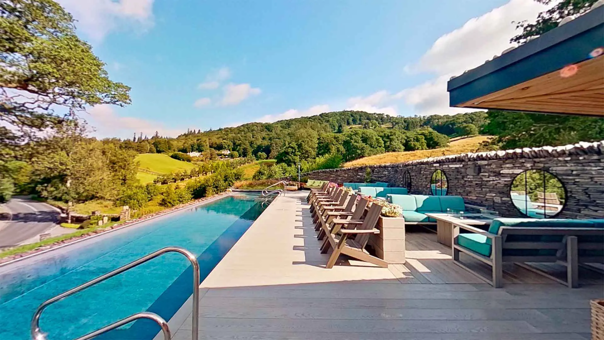 Spectacular infinity-edge vitality pool at Low Wood Bay Resort and Spa on the shores of Lake Windermere, featuring panoramic Lake District mountain views, traditional Lakeland dry stone walling, wooden sun loungers, and outdoor relaxation areas perfect for spa days